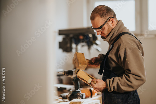 Schilderij op canvas A carpenter wearing safety glasses planes a wooden block with a mallet and hand plane