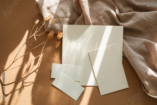 Aesthetic flat lay of textured paper mockups, linen fabric, and dried flowers in sunlight.