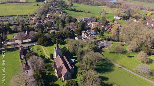 Hertingfordbury village drone pullback reveals parish church, cottages and treelined lanes amid lush Hertfordshire countryside on a bright day, widening to show rural landscape.