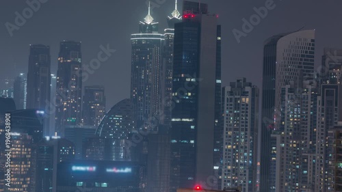 Bright illuminated skyscrapers with glowing lights in windows in the Dubai Business Bay district at night. Aerial top view of glowing downtown architecture in time-lapse.