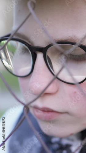 Sad teenage boy near fence after school, theme of bullying. Vertical video.