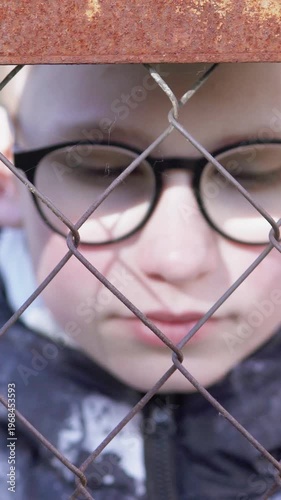 Sad teenage boy near fence after school, theme of bullying. Vertical video.