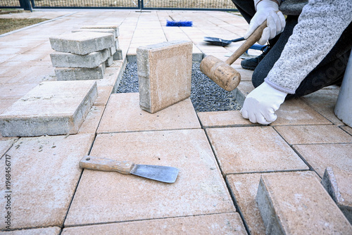 Worker installing concrete paving slabs on a gravel base during outdoor hardscaping project