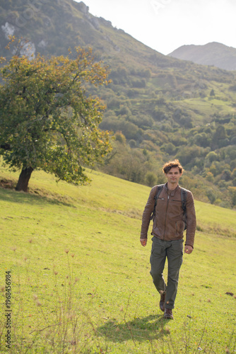  Young man hiking on a green mountain slope in Asturias, Spain, at sunny autumn day
