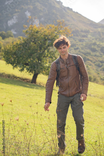  Young man hiking on a green mountain slope in Asturias, Spain, at sunny autumn day
