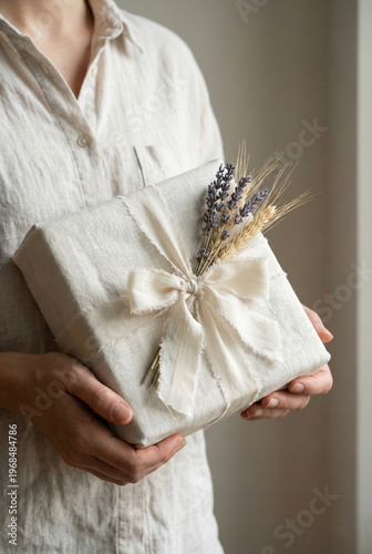 Hands Holding Sustainably Wrapped Gift In Linen Fabric With Dried Lavender And Frayed Ribbon Detail