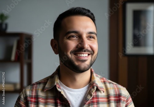 Happy man with beard smiling and looking away indoors with he is wearing a plaid shirt over a