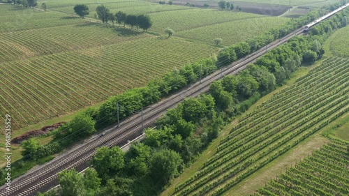 A red high-speed train streaks across the Italian landscape, weaving through vineyards in a stunning top-down view.