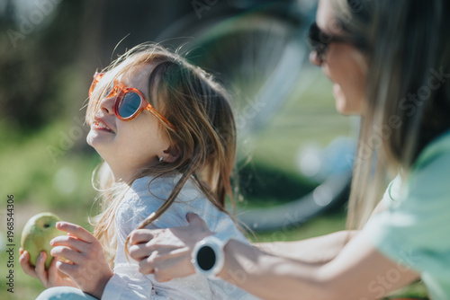 Fotografie A mother and young daughter share a joyful outdoor moment as the girl holds an apple
