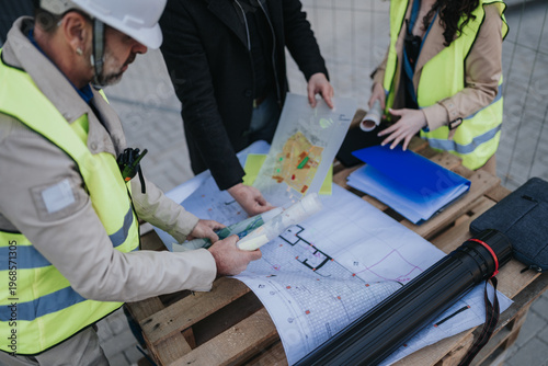 Photos Construction engineers in safety vests examine blueprints and site plans on a wooden pallet