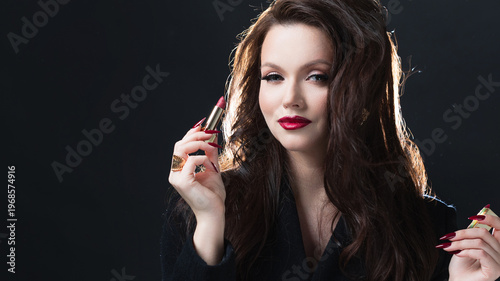 Elegant brunette holding red lipstick, dark studio