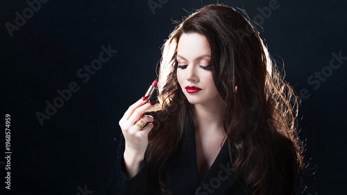 Luxurious brunette applying red lipstick, dark studio