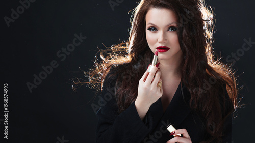 Elegant brunette holding red lipstick, dark studio