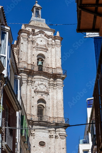 Majestic bell tower rising above narrow streets in Malaga, Spain, under a brilliant blue sky during midday