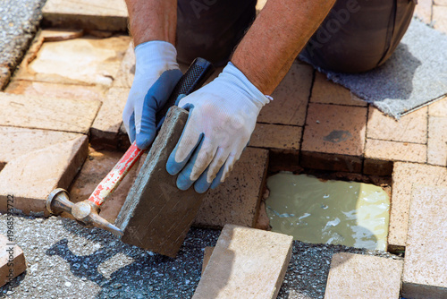 Contactor worker uses hammer to place bricks on walkway during patio repairing surface pavement