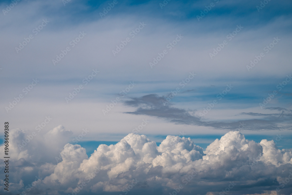 Fototapeta premium a dramatic layer of bright white, fluffy cumulus clouds at the bottom, topped by soft, wispy cirrus and grey cloud formations