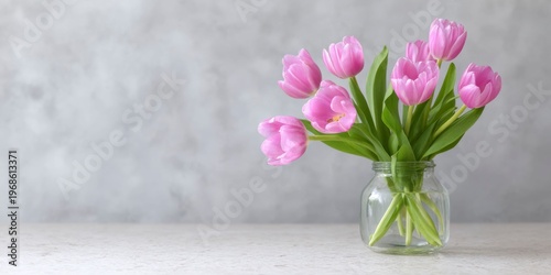 pink tulips in a glass vase on a table against a gray background