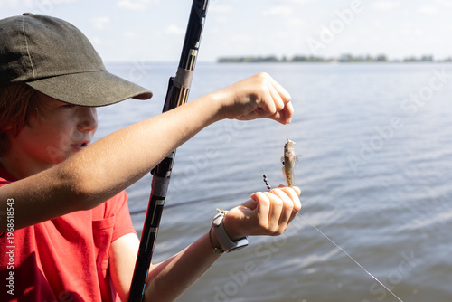 preteen boy caught a small fish on a fishing rod while standing by the river. Relaxation and favorite hobby by the water. Fishing vacation.