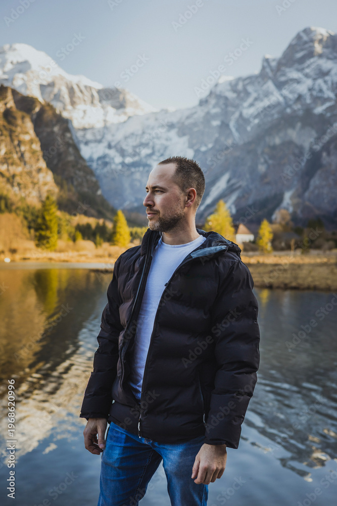 Fototapeta premium Man standing by alpine lake with mountain backdrop – outdoor lifestyle and travel concept