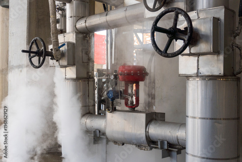 Steam coming out of pipes and valves. The valves are red and black. The steam is hot and thick