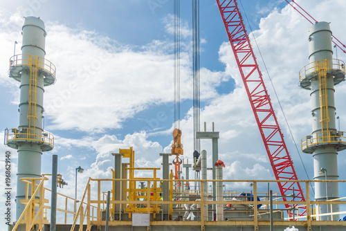 Crane is lifting a large object at a construction site. The crane is red and yellow. The sky is blue and cloudy