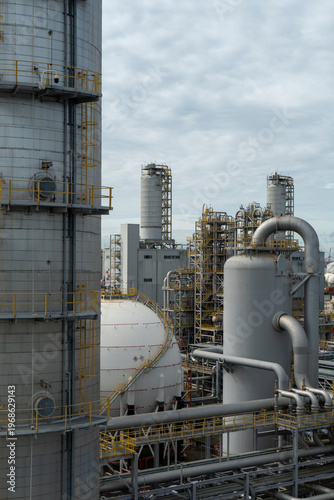 Large industrial plant with many tall structures and pipes. The sky is cloudy and the atmosphere is industrial