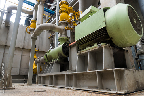 Large green machine with yellow valves sits on a grey platform. The machine is surrounded by pipes and valves, and it is a part of a larger industrial system. Concept of complexity and engineering