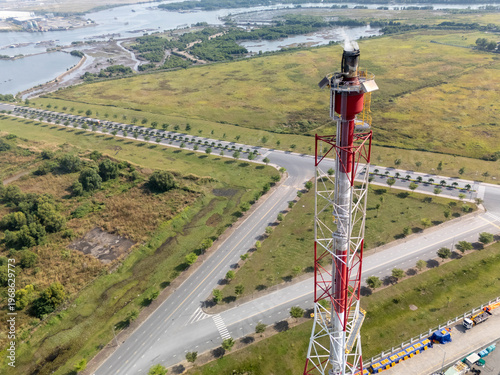 Tall red and white tower is seen in the distance. The tower is surrounded by a field and a road. The scene is peaceful and serene, with the tower standing tall
