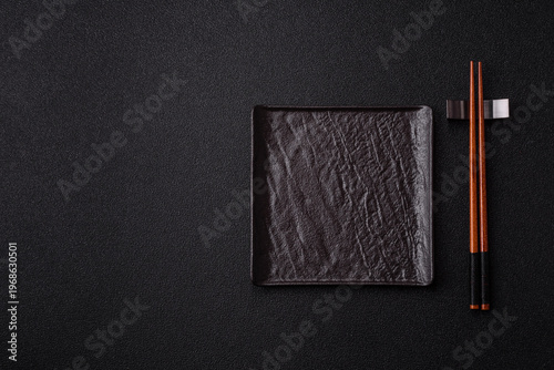 An empty ceramic square black plate with chopsticks for Asian food. An empty square plate
