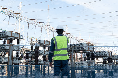 Bild auf Leinwand Engineer stands in a high voltage substation for grid monitoring, supporting power system inspection, asset reliability, operational safety, and utility infrastructure oversight