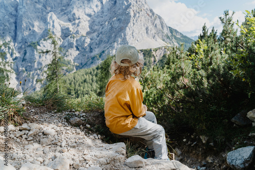 Foto Cute boy sitting on large rock near majestic mountains