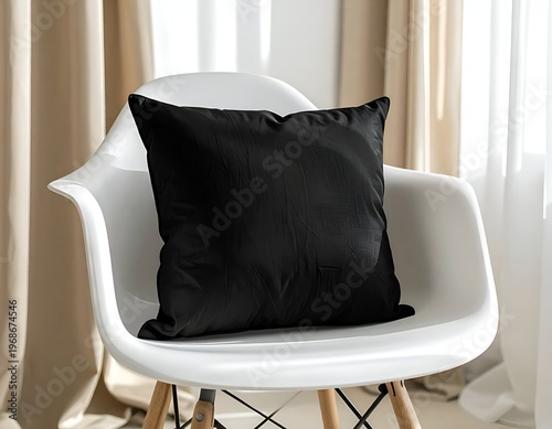 A black square pillow rests on a white modern chair, near a window with sheer beige curtains
