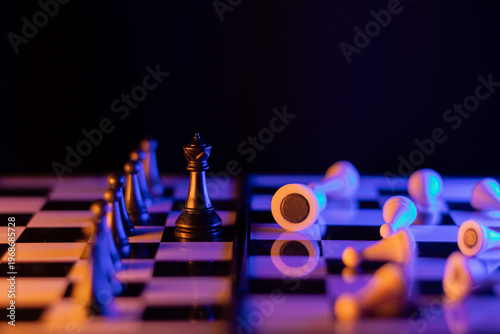 фотографія Chess queen illuminated in yellow and blue in front of toppled pieces, represent