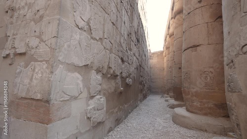 A narrow path between massive ancient stone columns with intricate hieroglyphic carvings at the historic Luxor Temple in Egypt.