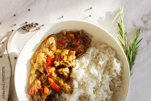 Savory meat and red bell pepper stew with creamy sauce and fluffy white rice, garnished with rosemary on a sunlit marble counter