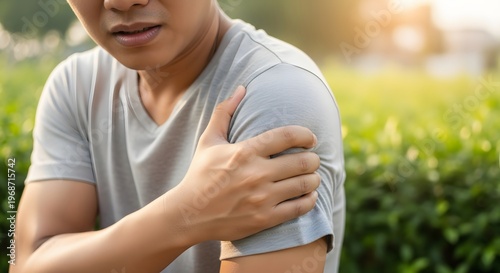 Man suffering from acute shoulder pain and muscle strain. Sports injury and physical therapy. Young man holding his painful shoulder while standing outdoors
