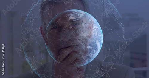 Thinking exec viewing hologram Earth mesh hand at chin in office wearing suit jacket collared shirt