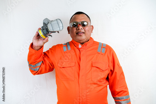 Man Wearing an Orange Safety Uniform and Protective Glasses Holding a Respirator Mask Ready for Hazardous Work in an Industrial Setting on a White Studio Background