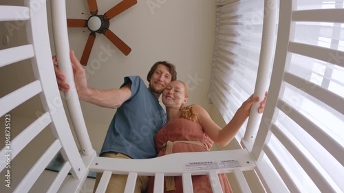 Smiling mother and father hugging and looking at their newborn in a crib, filmed from baby point of view. Tender family moment full of love and care. Parenthood, bonding and newborn care concept