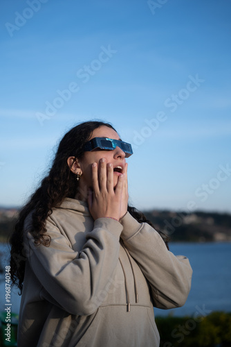 Teenage girl observing a solar eclipse with protective glasses outdoors, vertical  photo
