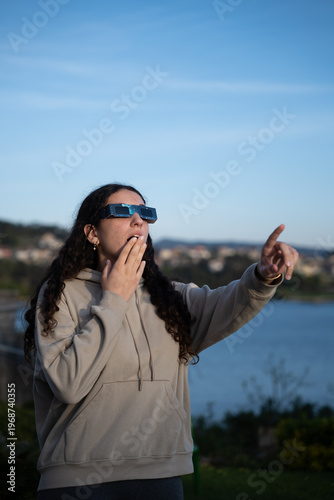 Teenage girl observing a solar eclipse with protective glasses outdoors, vertical image 