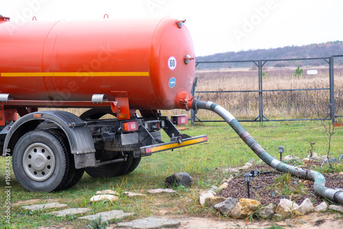 Sewage vacuum truck pumping waste from private house septic tank, liquid waste removal and disposal service, sanitation business concept.