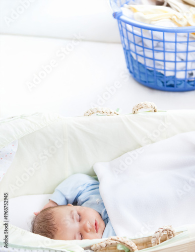 Tableau sur toile Infant male sleeping in padded bassinet in nursery under white blanket, wearing