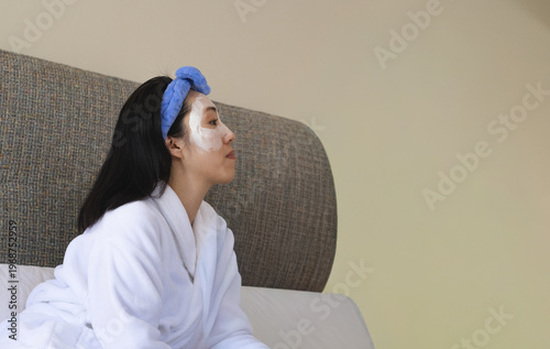 Woman in robe blue headband sitting wearing facial mask causing animated skin analysis for skincare