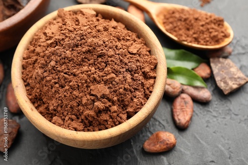 Cocoa powder in bowl, beans and pieces of chocolate on dark textured table, closeup