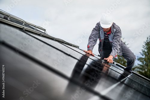 Man technician mounting photovoltaic solar panels on roof of house with help of hex key.
