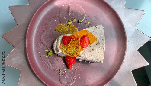 Elegant fruit dessert with cream, strawberry, orange and physalis garnished with pistachio on purple plate