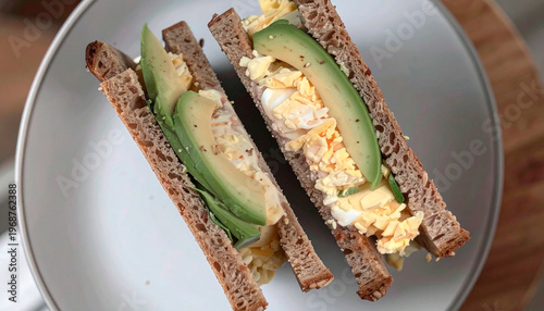Healthy avocado and scrambled egg sandwich on dark rye bread cut in half on plate