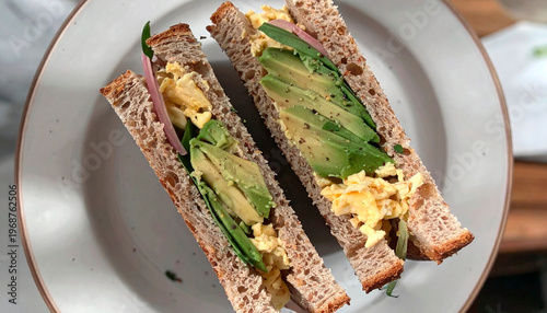 Healthy avocado and scrambled egg sandwich on dark rye bread cut in half on plate