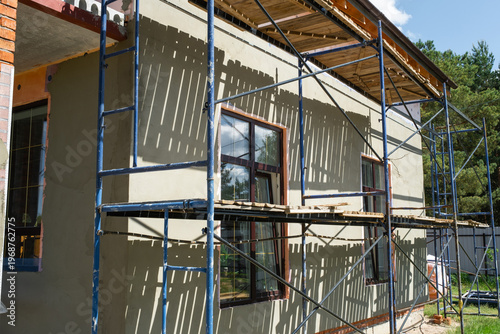 Plaster finish on exterior wall, facade mesh, scaffolding setup, wall protection, smoothing, insulation layer, construction completion, repair, decorative stage.